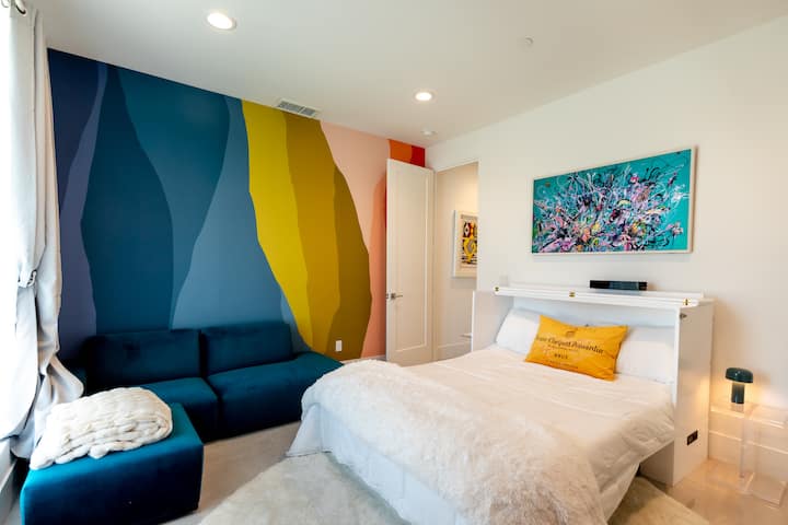 Guest room with the queen bed pulled out, a teal sectional and a blue and yellow color-block mural