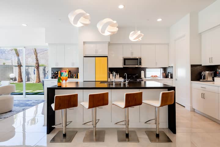 White kitchen with a black island, four leather stools and a yellow glass-door refrigerator