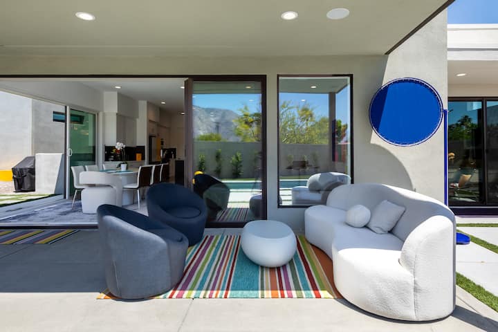 Covered patio lounge with a white bouclé sofa and swivel chairs, just outside the great room's glass doors