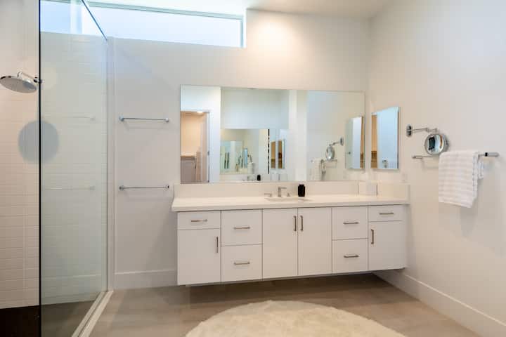 Primary bathroom with a long white vanity, two sinks and a glass-walled shower