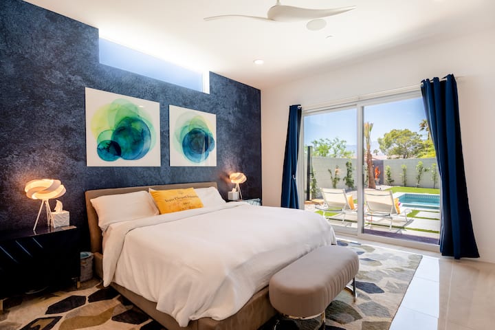 Primary bedroom with a king bed, blue-green art on a dark feature wall and a glass door to the pool