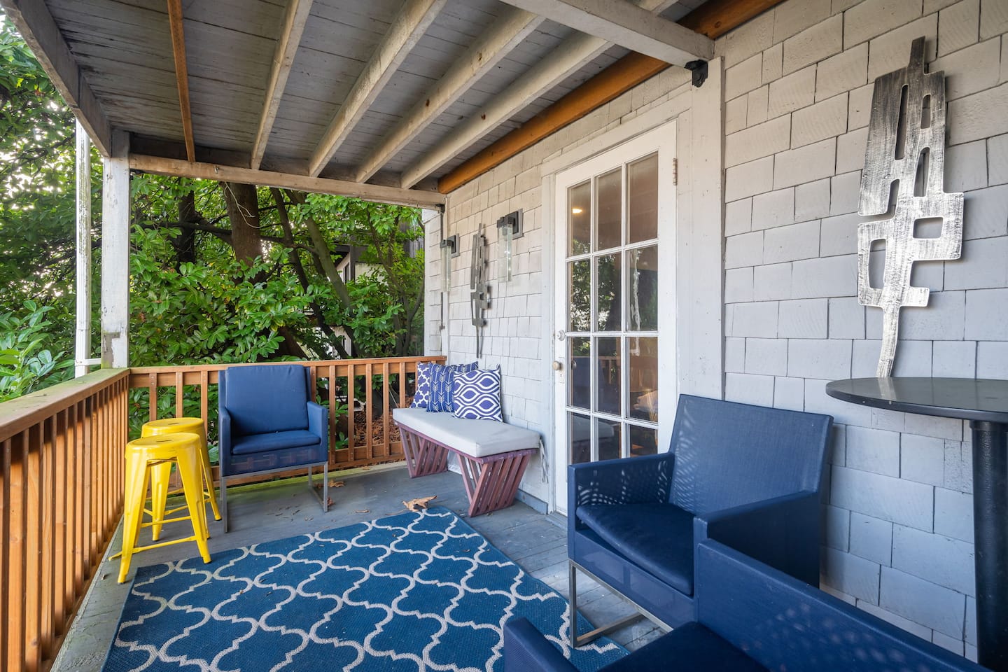 Covered balcony with blue chairs, a rug and bright yellow stools
